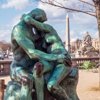 Bronze statue The Kiss by Auguste Rodin (1882) in the Tuileries Garden with Egyptian obelisk in background - Paris, France