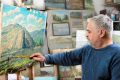 older white artist adding finishes touches to naturescape painting in art studio