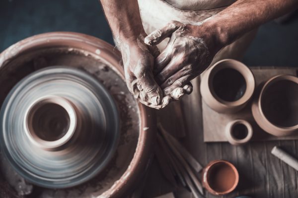 Top view of potter standing near pottery wheel and holding hands together in crafts studio